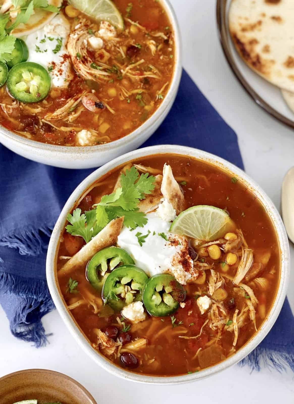 two bowls of chicken taco soup with jalepenos and chicken and sour cream garnish