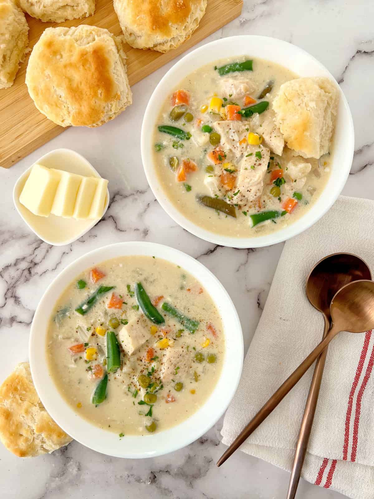 chicken pot pie soup in bowls with biscuits on side 