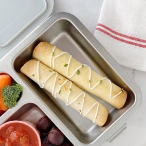 taquitos in a lunch box with grapes and fruit