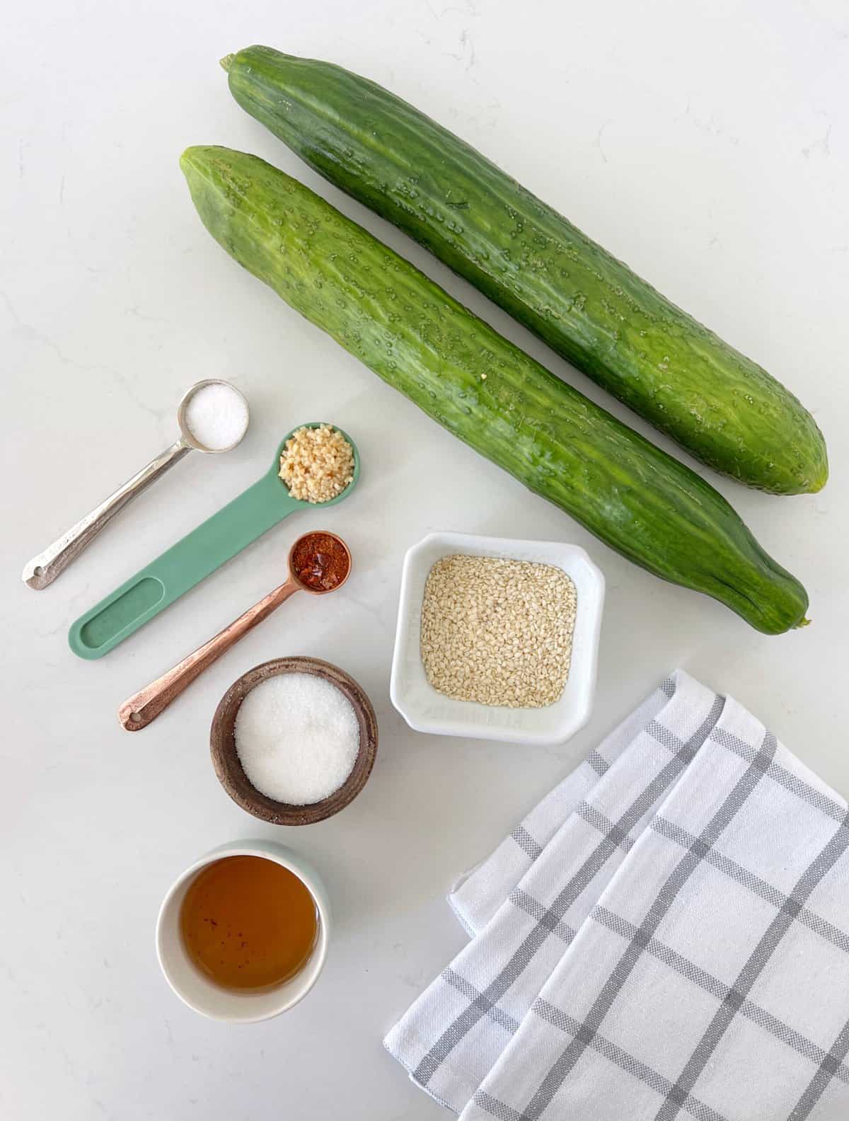 cucumbers and spices in bowls and measuring cups next to a kitchen towel 