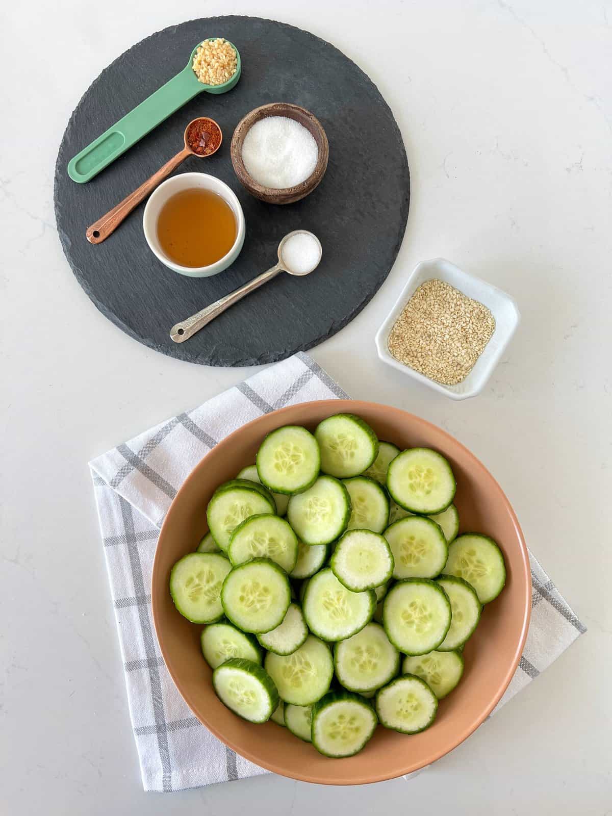 photo of seasonings next to cucumber in a bowl and sesame sees 