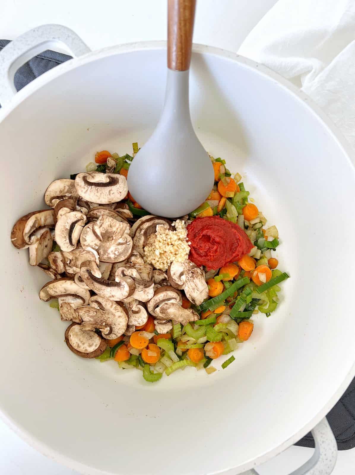veggies and mushrooms in a pan with a gray spatula 