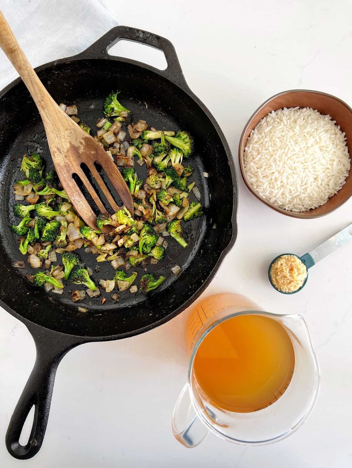 broccoli and onion in skillet next to broth and rice 
