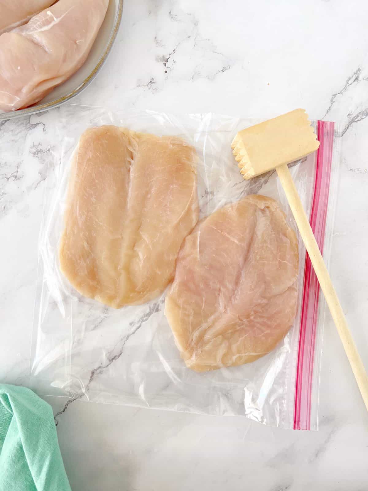 chicken breasts in ziplock bag with meat pounder on top 