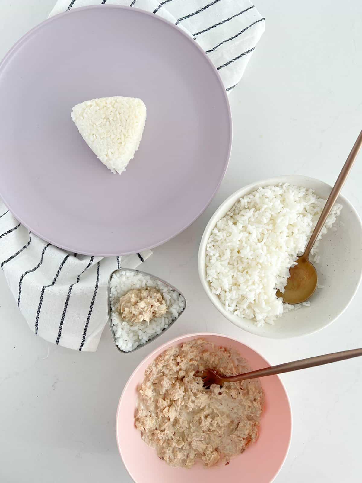 triangle mold rice on a purple plat with rice on side and tuna 