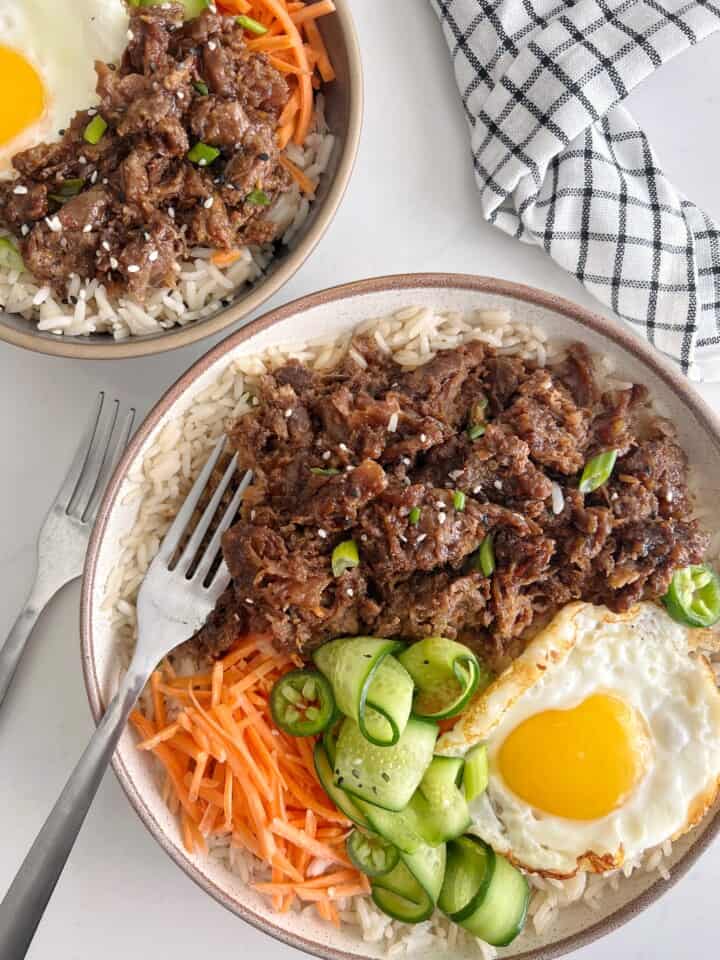 bowls of beef bowl and rice with carrots cucumber and egg